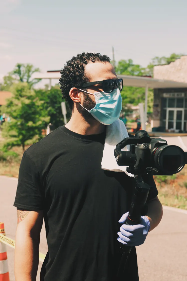 Me in a surgical mask, sunglasses and blue gloves, camera in one hand, at the roadside during the 2020 food drive.