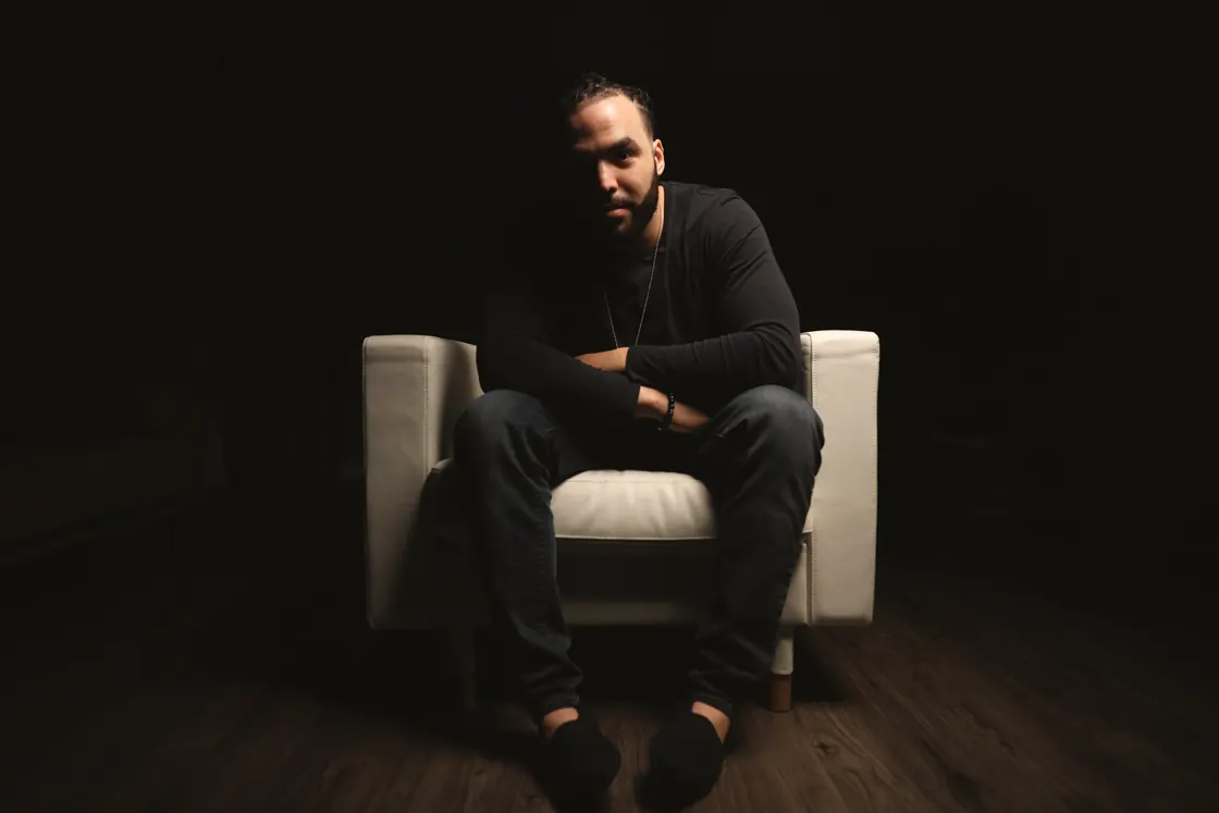 Me in a white armchair in a blacked-out room, one light, everything else cleared away.