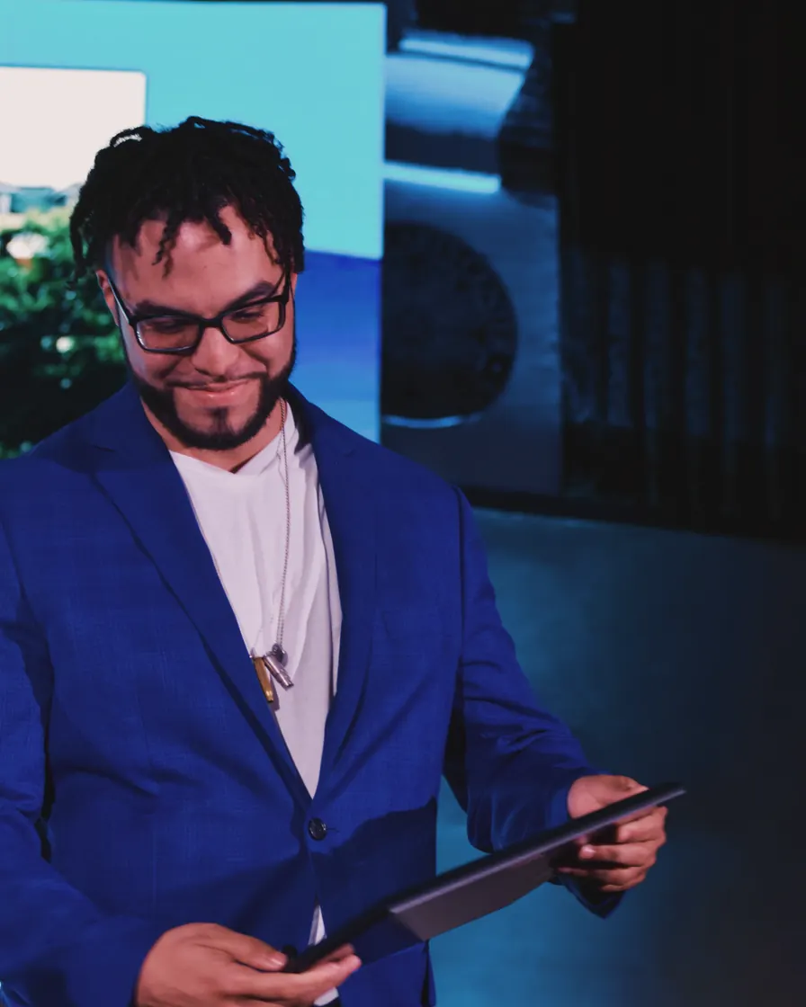 Me in a blue suit on stage with the award in my hands, looking down at it.