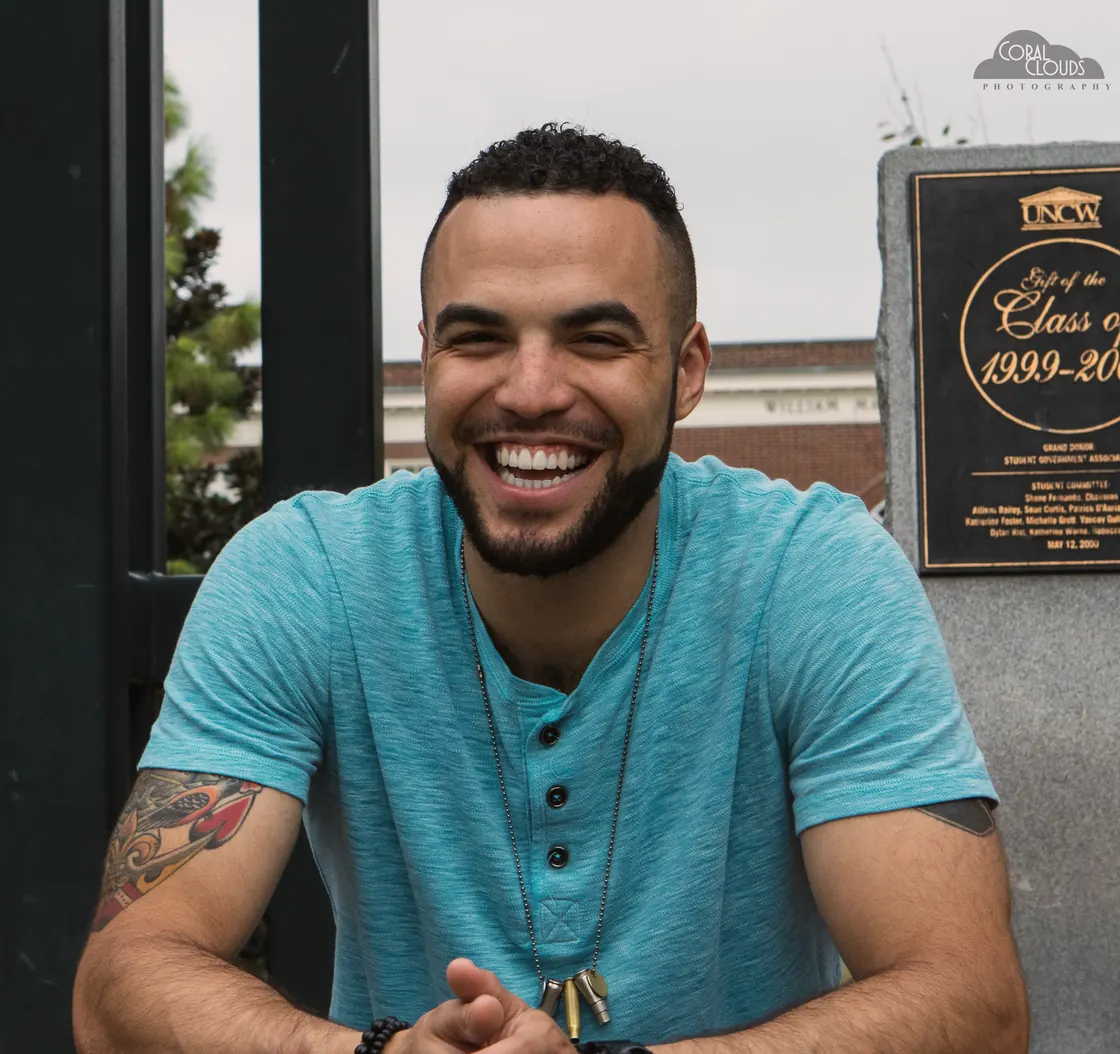 Me at a UNCW gate, laughing, the class plaque behind me.